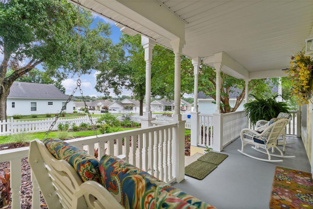 A covered front porch features a hanging swing, white railings, and two white rocking chairs — 1622 LAUREL WAY, TAVARES, FL