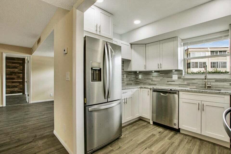 A kitchen features white cabinets, stainless steel appliances, granite countertops, and wood-look flooring — 705 Lori Drive # 104, Palm Springs FL 33461, PALM SPRINGS, FL
