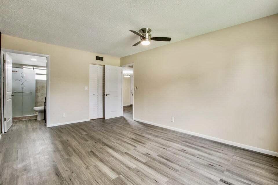A bedroom with light beige walls, gray wood-look flooring, a ceiling fan, and an attached bathroom — 705 Lori Drive # 104, Palm Springs FL 33461, PALM SPRINGS, FL