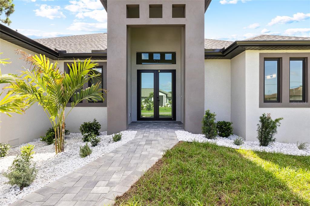 The exterior of a modern house features a paved walkway leading to double glass doors — 260 TOURNAMENT ROAD, ROTONDA WEST, FL
