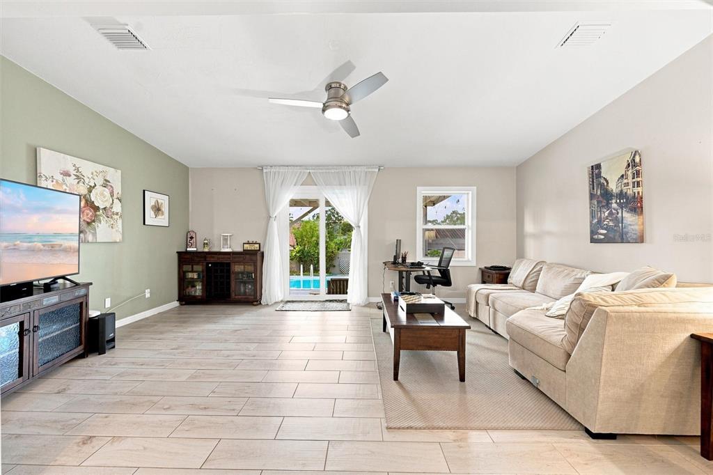 A living room features light wood-look tile flooring, a ceiling fan, and a sliding glass door — 670 KIRKLAND CIRCLE, DUNEDIN, FL