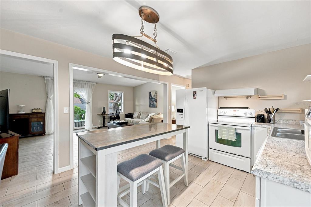 A kitchen with a wooden island, white appliances, and light tile flooring opens to a living area — 670 KIRKLAND CIRCLE, DUNEDIN, FL