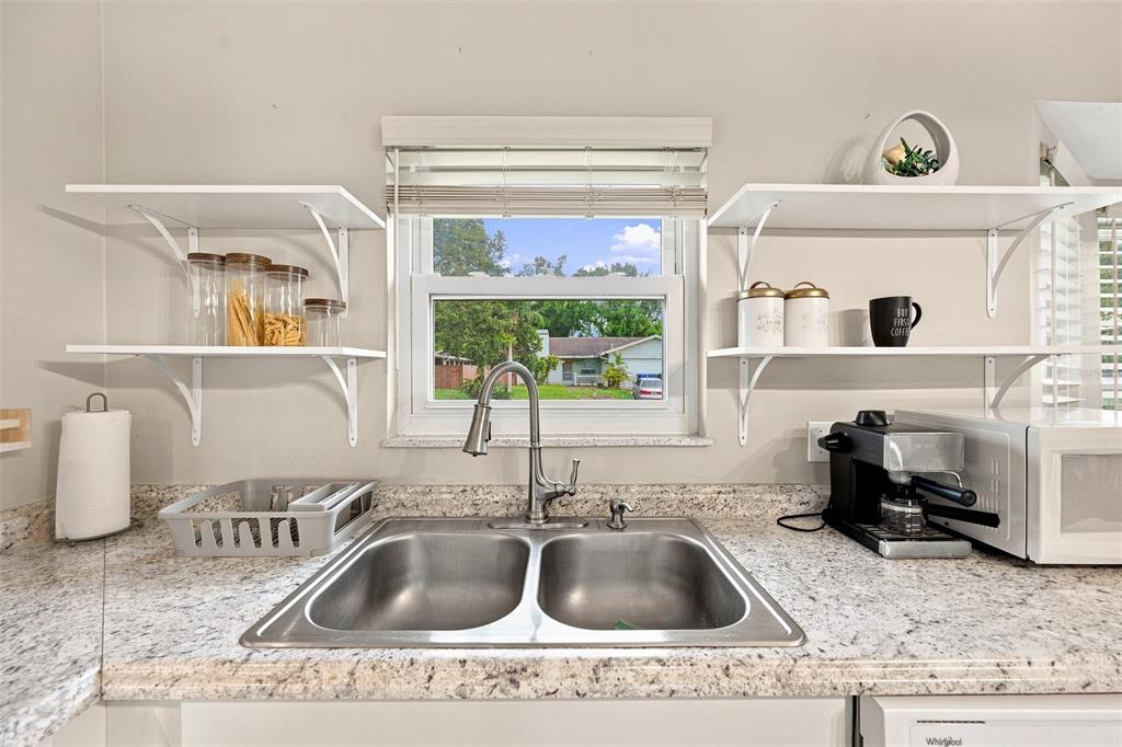 A kitchen sink area features granite countertops, white open shelving, and a window view — 670 KIRKLAND CIRCLE, DUNEDIN, FL