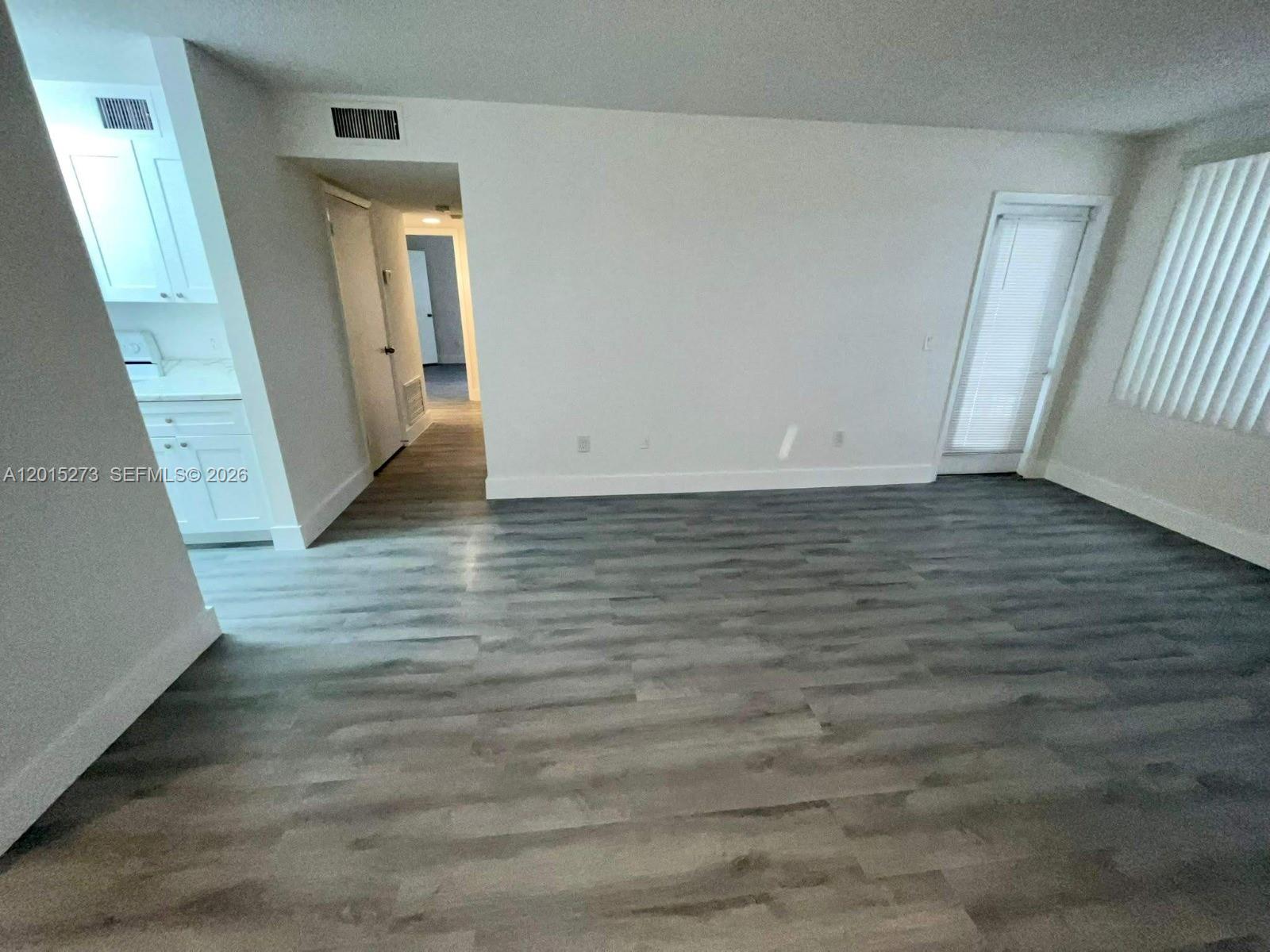 An empty room features gray wood-look flooring, white walls, and a doorway to a kitchen — 4561 W Mcnab Rd # 17, Pompano Beach FL 33069, POMPANO BEACH, FL