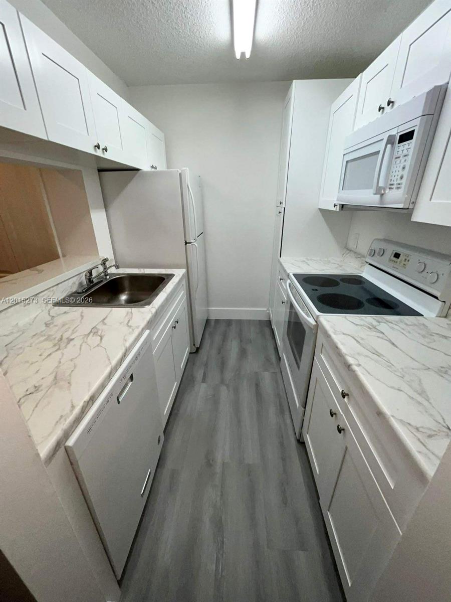 A galley kitchen features white cabinets, marble-patterned countertops, stainless steel appliances, and gray flooring — 4561 W Mcnab Rd # 17, Pompano Beach FL 33069, POMPANO BEACH, FL