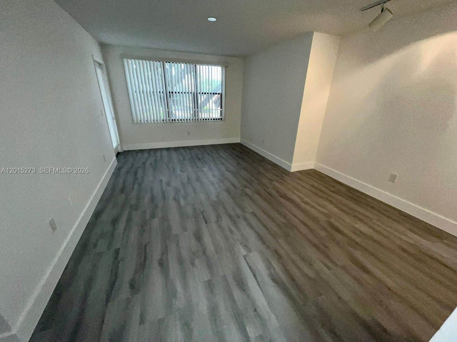 An empty room features white walls, a large window with blinds, and wood-look flooring — 4561 W Mcnab Rd # 17, Pompano Beach FL 33069, POMPANO BEACH, FL