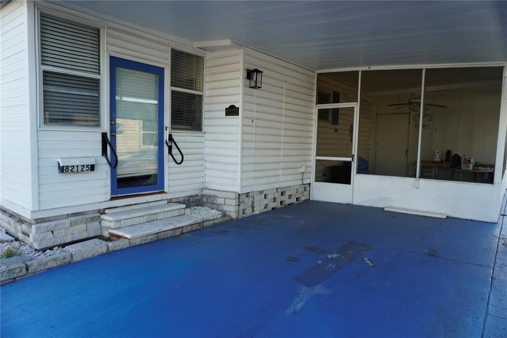 A blue-painted carport leads to a white-sided home with a blue front door — 82125 B STREET N UNIT 125, PINELLAS PARK, FL