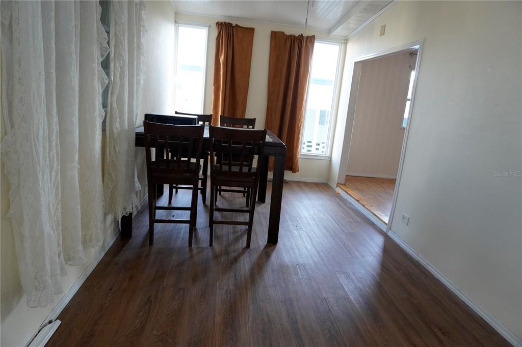 A dining area features wood-look flooring, a dark wood table with chairs, and two windows — 82125 B STREET N UNIT 125, PINELLAS PARK, FL