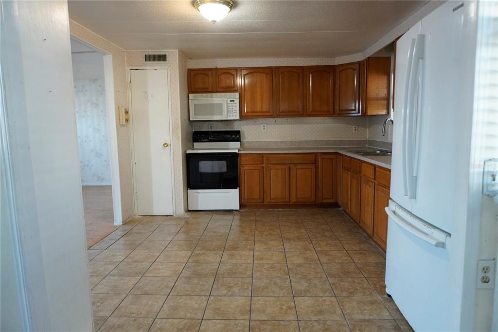 A kitchen with wood cabinets, white appliances, and tan tile flooring — 82125 B STREET N UNIT 125, PINELLAS PARK, FL