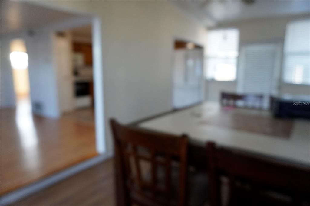 A blurry view of a dining area with wooden chairs and a kitchen in the background — 82125 B STREET N UNIT 125, PINELLAS PARK, FL