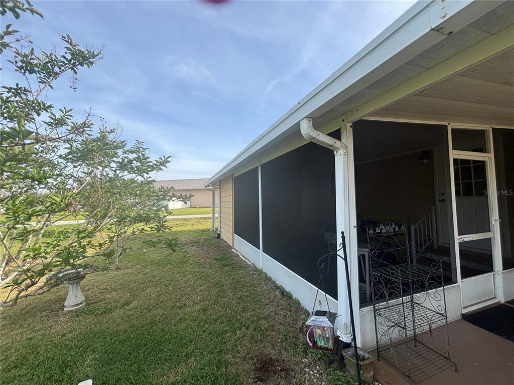 A screened-in porch with a metal frame sits beside a grassy yard and tree — 3963 PARWAY ROAD UNIT 1325, ZELLWOOD, FL