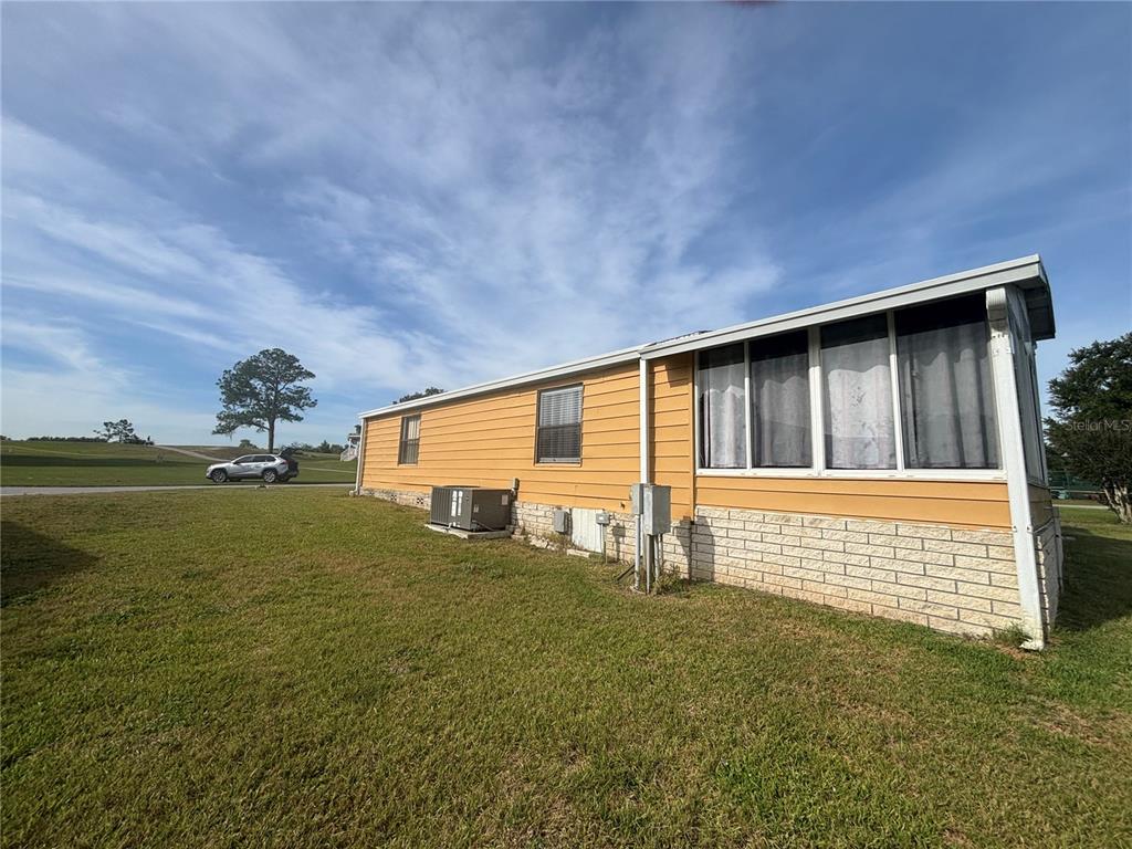 A side view of a yellow mobile home with a brick base and screened porch — 3963 PARWAY ROAD UNIT 1325, ZELLWOOD, FL
