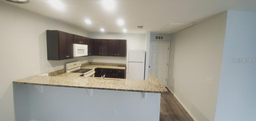 A kitchen with dark wood cabinets, granite countertops, white appliances, and a breakfast bar — 284 GARDNER LANE UNIT E, KISSIMMEE, FL