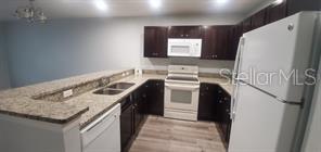 A kitchen features dark wood cabinets, granite countertops, and white appliances — 284 GARDNER LANE UNIT E, KISSIMMEE, FL