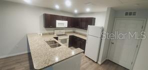 A kitchen features dark wood cabinets, light granite countertops, a white refrigerator, and light flooring — 284 GARDNER LANE UNIT E, KISSIMMEE, FL