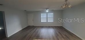 An empty room features light gray walls, wood-look flooring, a ceiling fan, and a chandelier — 284 GARDNER LANE UNIT E, KISSIMMEE, FL