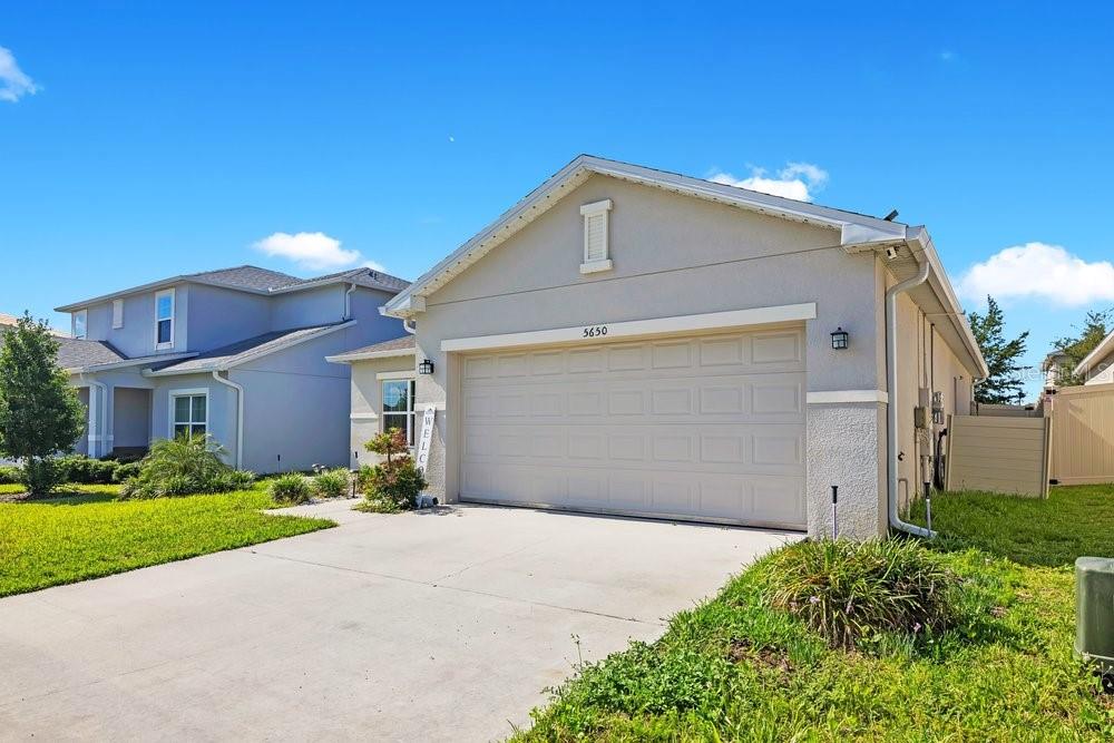 A single-story house with a beige stucco exterior, a two-car garage, and a concrete driveway — 5650 COSTA BLANCA WAY, DAVENPORT, FL