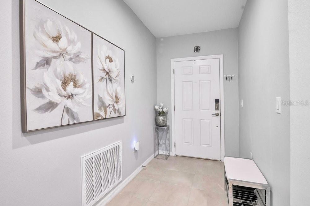 An entryway features light gray walls, tile flooring, a white door, and floral wall art — 5650 COSTA BLANCA WAY, DAVENPORT, FL