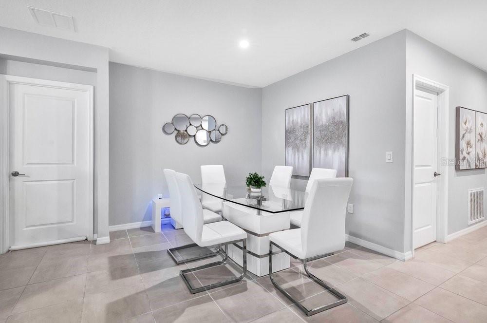 A dining room with a glass table, white chairs, tile flooring, and wall art — 5650 COSTA BLANCA WAY, DAVENPORT, FL