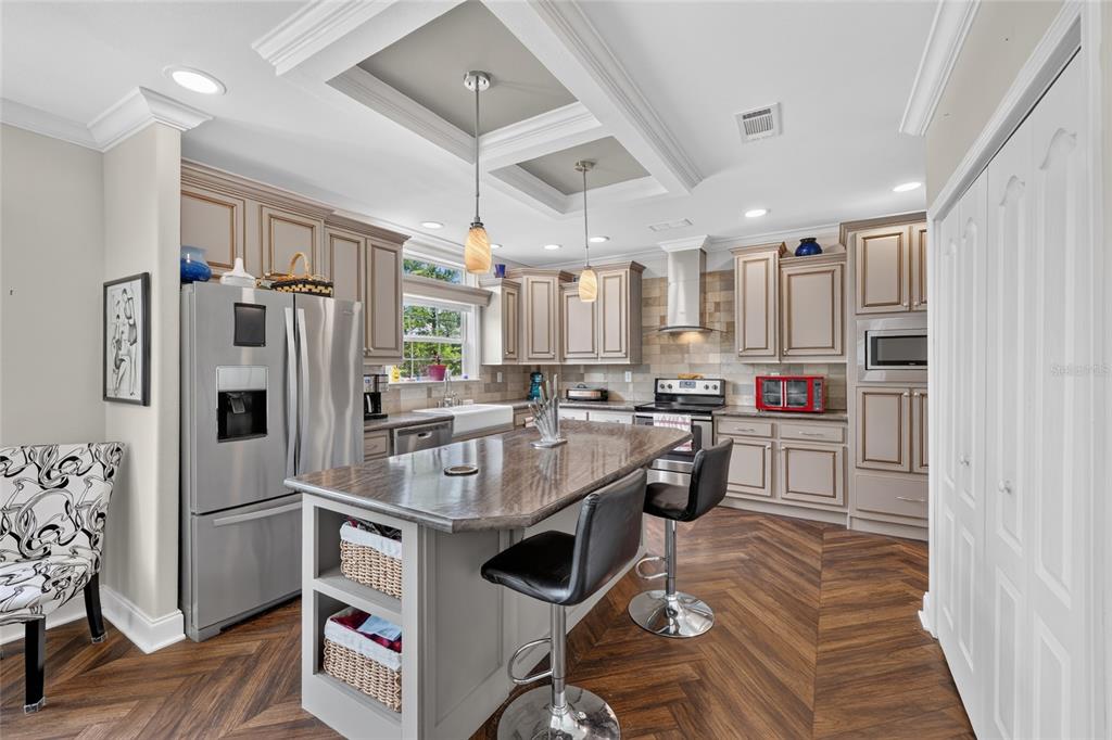 A kitchen features a central island with bar stools, stainless steel appliances, and wood-look flooring — 7131 NE 138TH TERRACE, WILLISTON, FL