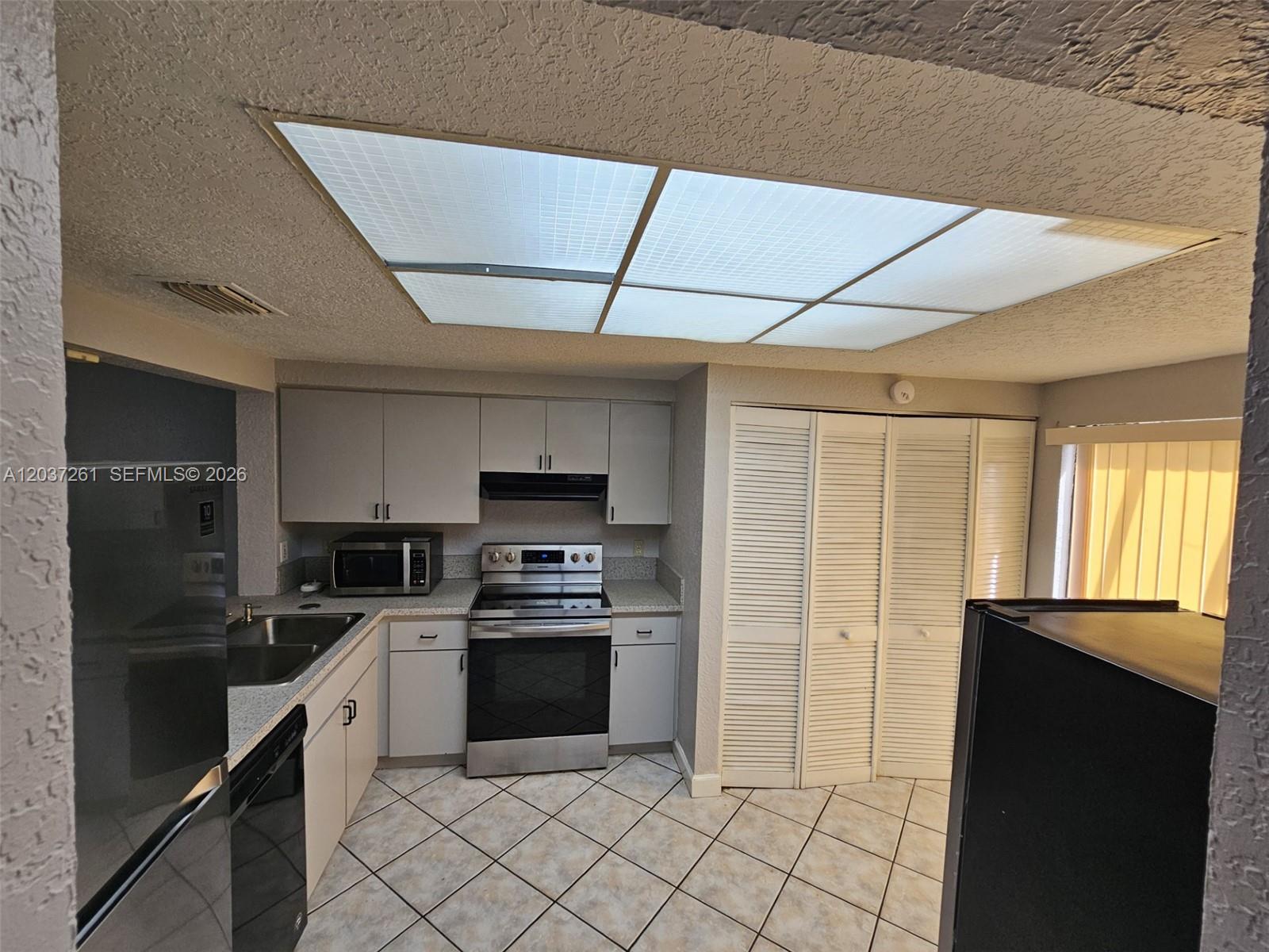 A kitchen features light gray cabinets, stainless steel appliances, tile flooring, and a large skylight — 8837 NW 48th St, Sunrise FL 33351, SUNRISE, FL