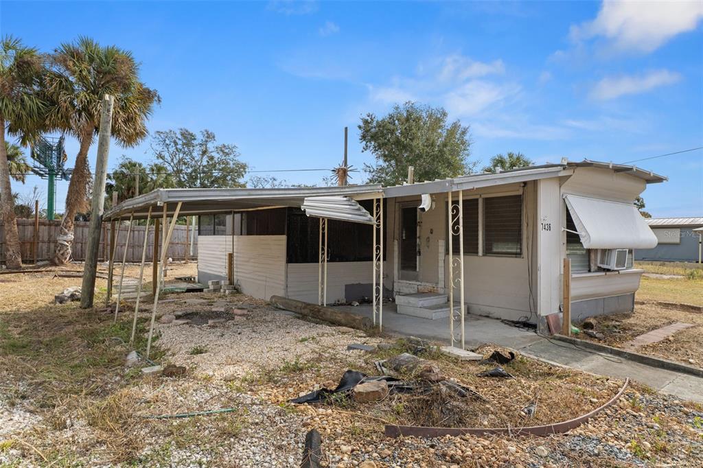 A single-story mobile home with a damaged metal carport and a gravel yard — 7436 VAGABOND DRIVE, NEW PORT RICHEY, FL