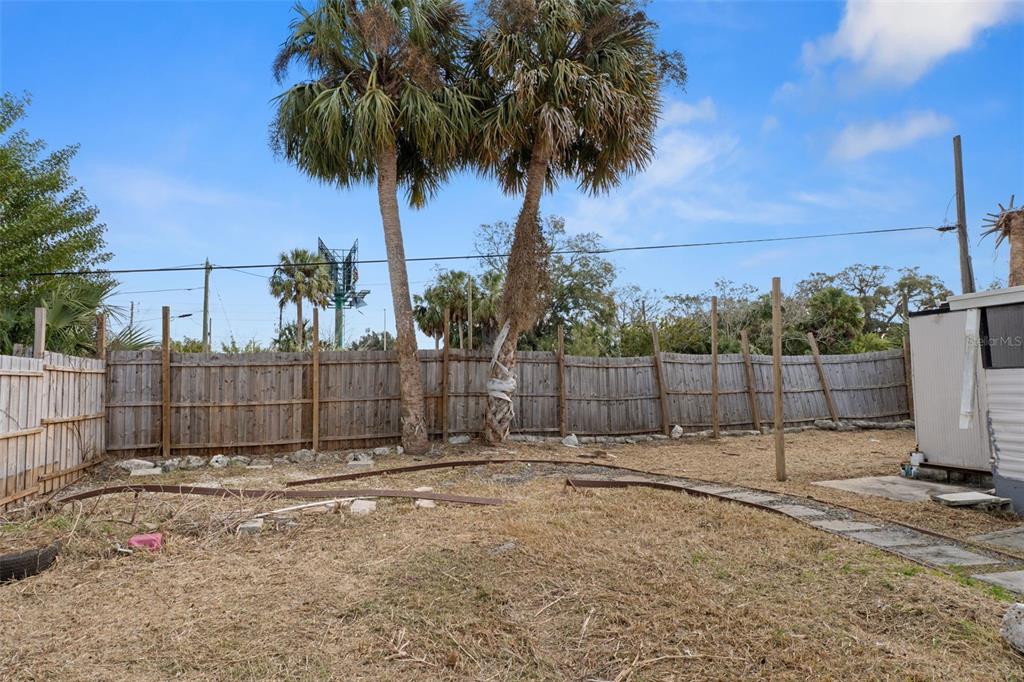 A fenced backyard features two tall palm trees, dry grass, and curved metal tracks — 7436 VAGABOND DRIVE, NEW PORT RICHEY, FL