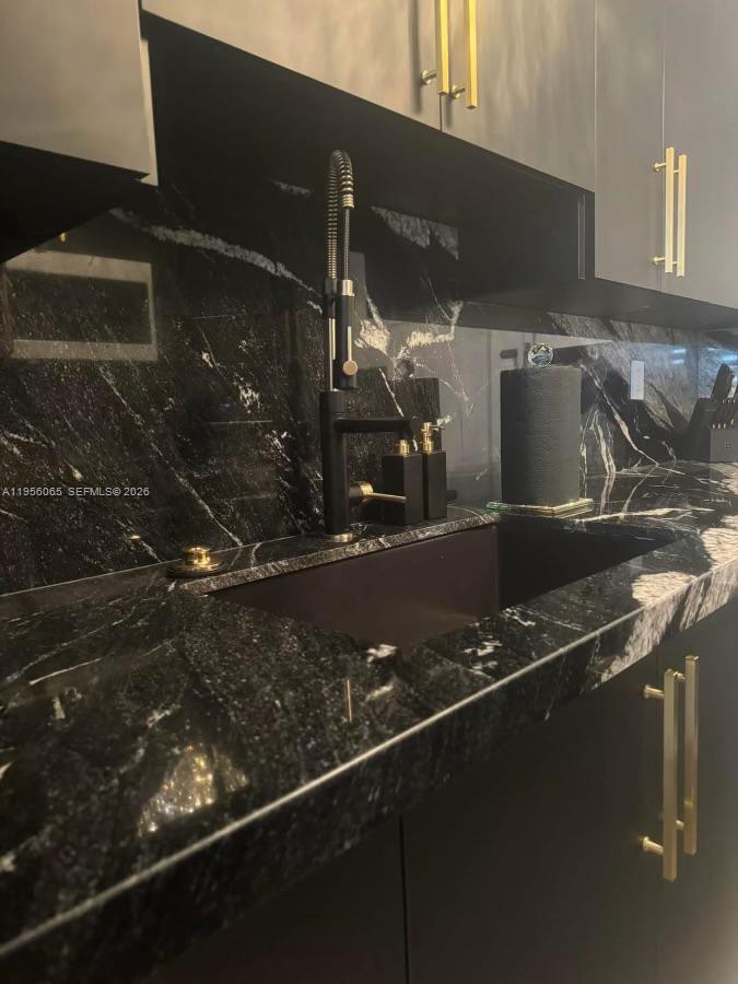 A modern kitchen features black marble countertops, a dark sink, and gold cabinet hardware — 100 Lincoln Rd # 408, Miami Beach FL 33139, MIAMI BEACH, FL