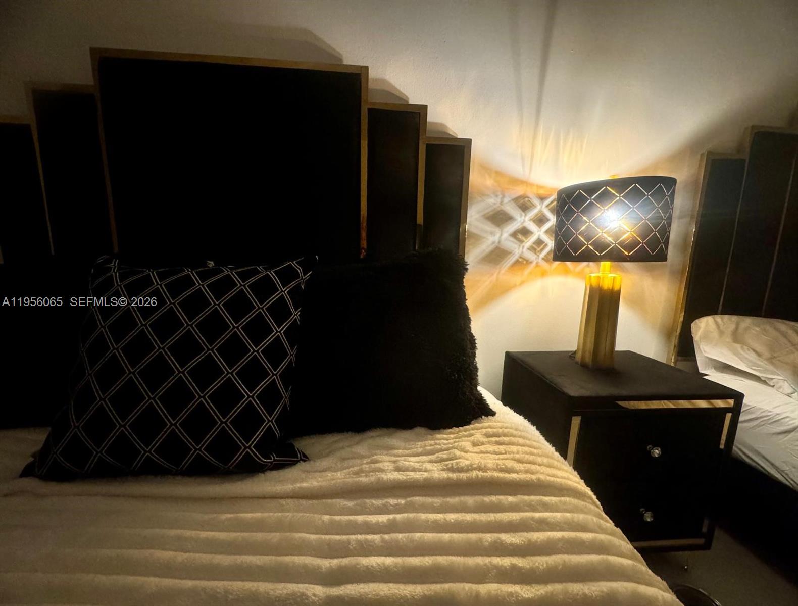 A bedroom features a black headboard, a patterned lamp, and a textured white blanket — 100 Lincoln Rd # 408, Miami Beach FL 33139, MIAMI BEACH, FL