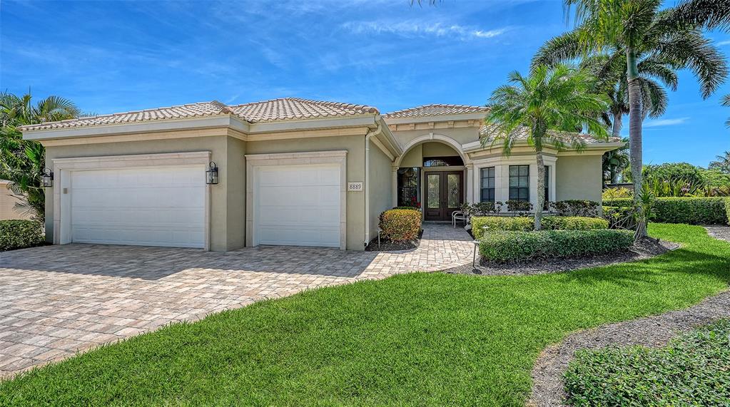 A single-story house with a beige stucco exterior, a paver driveway, and a three-car garage — 8889 ENCLAVE COURT, SARASOTA, FL