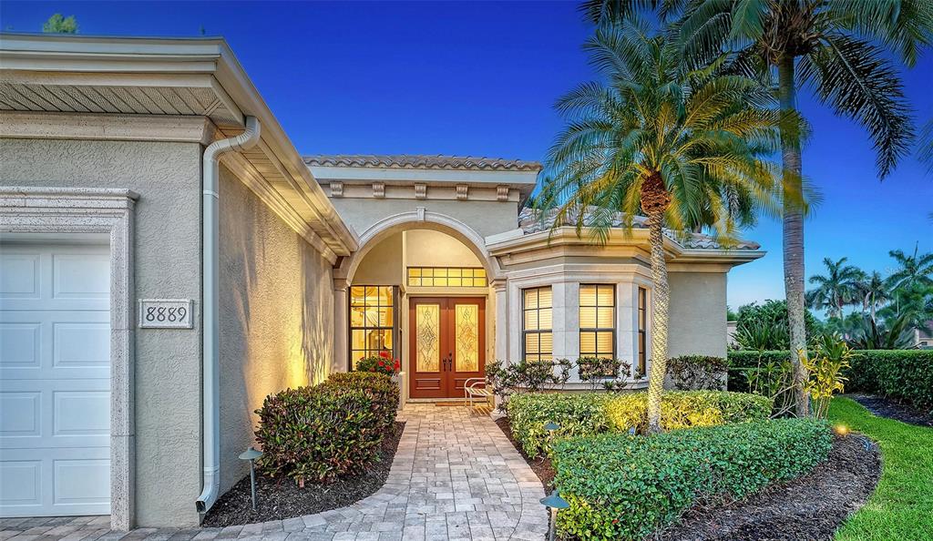 A beige stucco house features a paved walkway leading to double front doors under an arch — 8889 ENCLAVE COURT, SARASOTA, FL