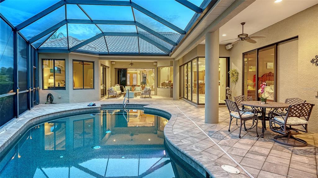 A screened-in patio features a curved swimming pool, tile flooring, and outdoor dining furniture — 8889 ENCLAVE COURT, SARASOTA, FL