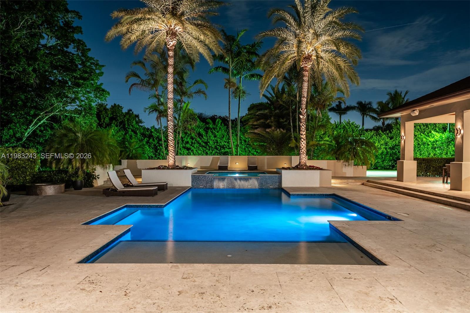A swimming pool with a spa and waterfall sits on a stone patio at night — 8967 SW 117th St, Miami FL 33176, MIAMI, FL