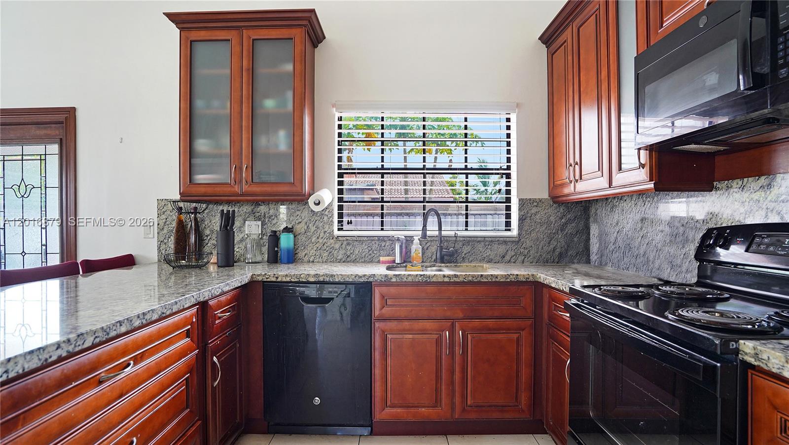 A kitchen features dark wood cabinets, granite countertops, a black dishwasher, and a window — 13755 SW 19th Ter, Miami FL 33175, MIAMI, FL