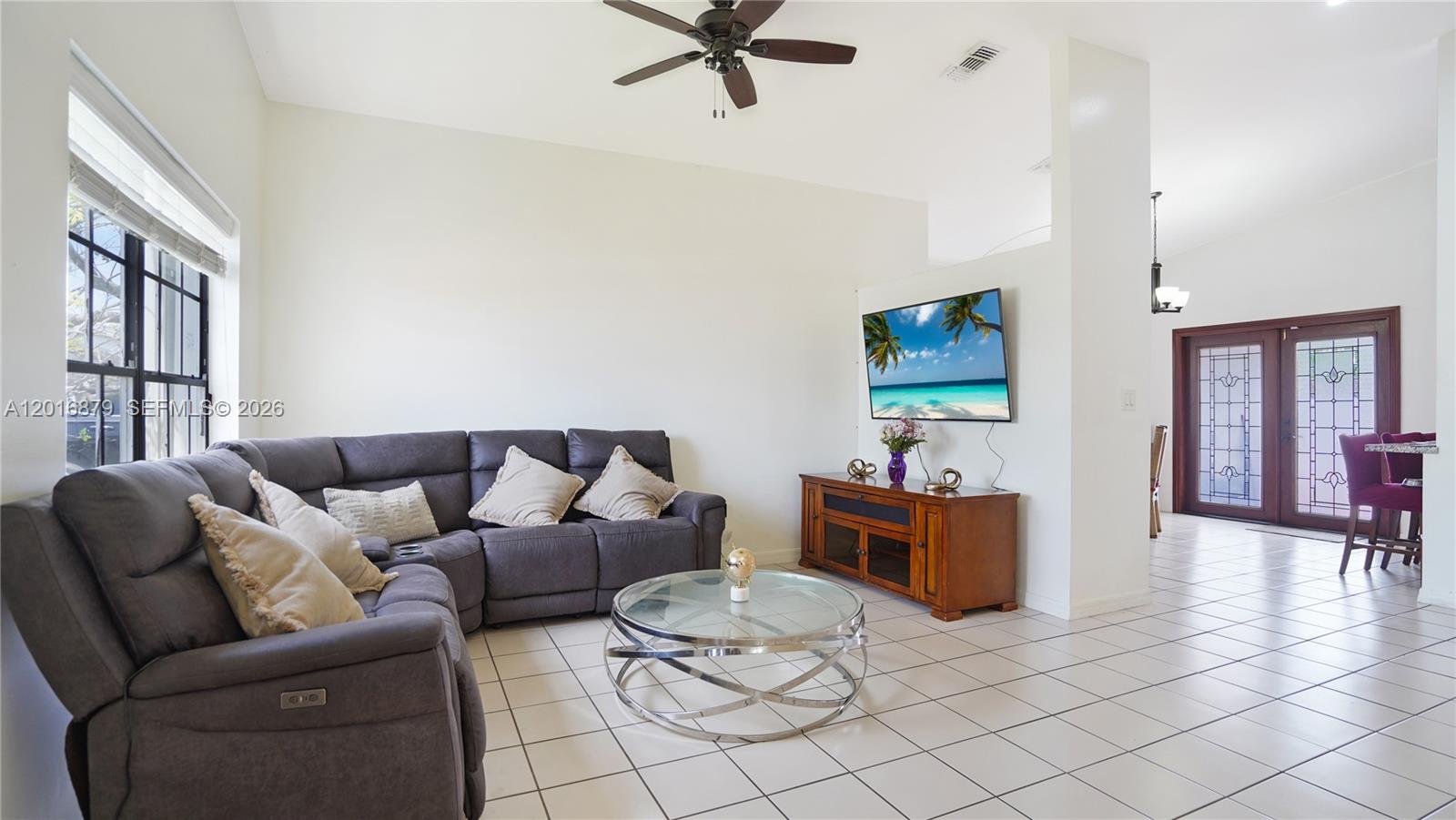 A living room features a grey sectional sofa, a glass coffee table, and a wall-mounted television — 13755 SW 19th Ter, Miami FL 33175, MIAMI, FL