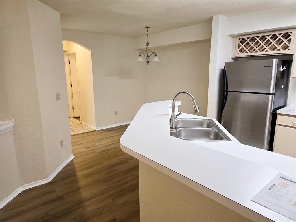 A kitchen with a white breakfast bar, stainless steel refrigerator, and wood-look flooring — 831 CAMARGO WAY UNIT 109, ALTAMONTE SPRINGS, FL