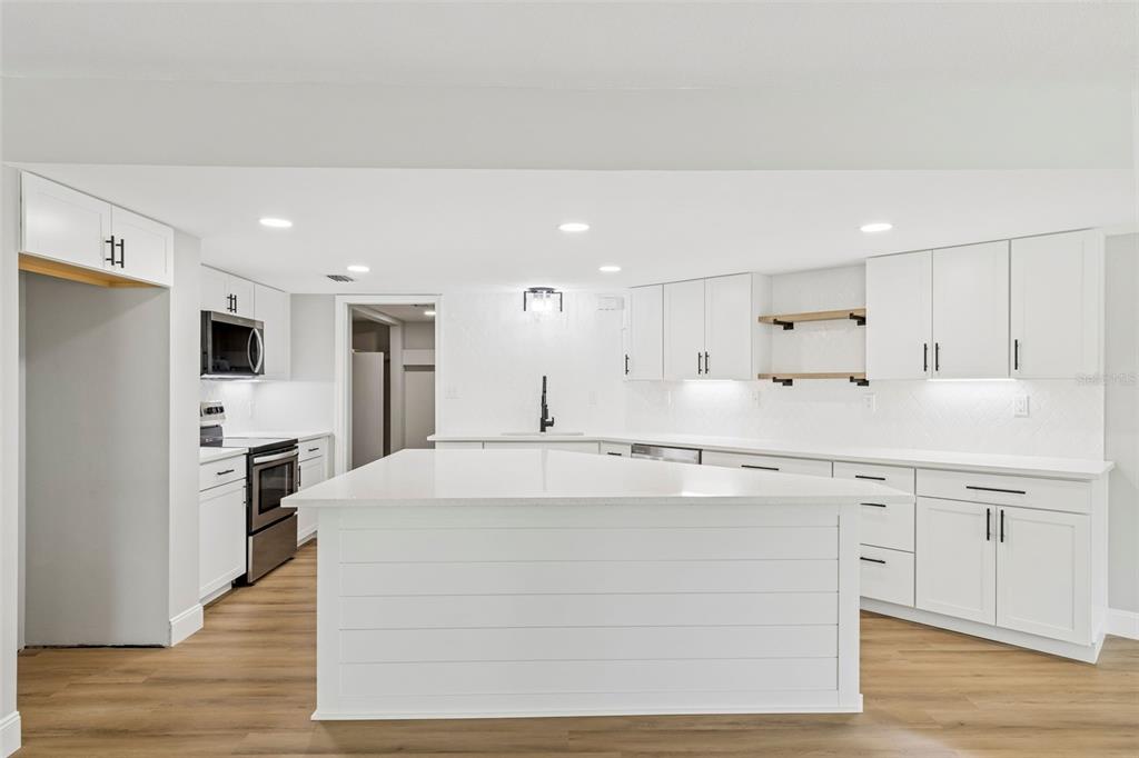 A modern kitchen features white cabinetry, a large central island, and light wood flooring — 2533 DOLLY BAY DRIVE UNIT 101, PALM HARBOR, FL