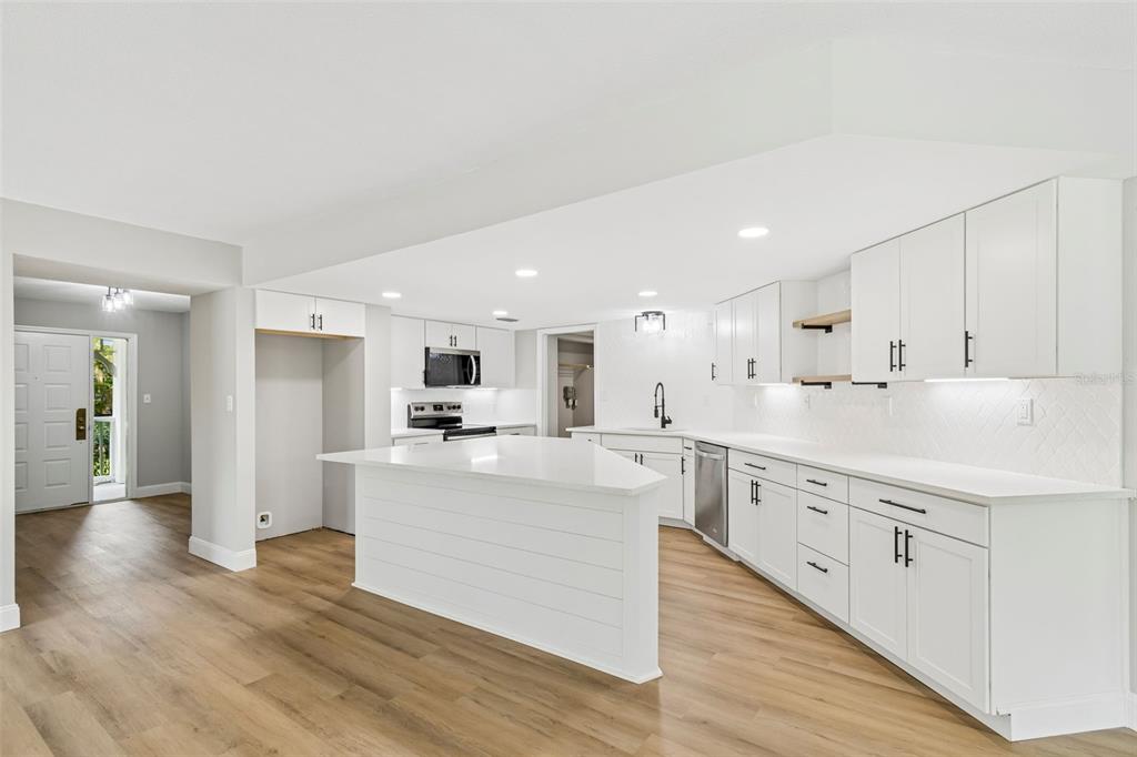 A modern white kitchen features a large island, shaker cabinets, and light wood-look flooring — 2533 DOLLY BAY DRIVE UNIT 101, PALM HARBOR, FL