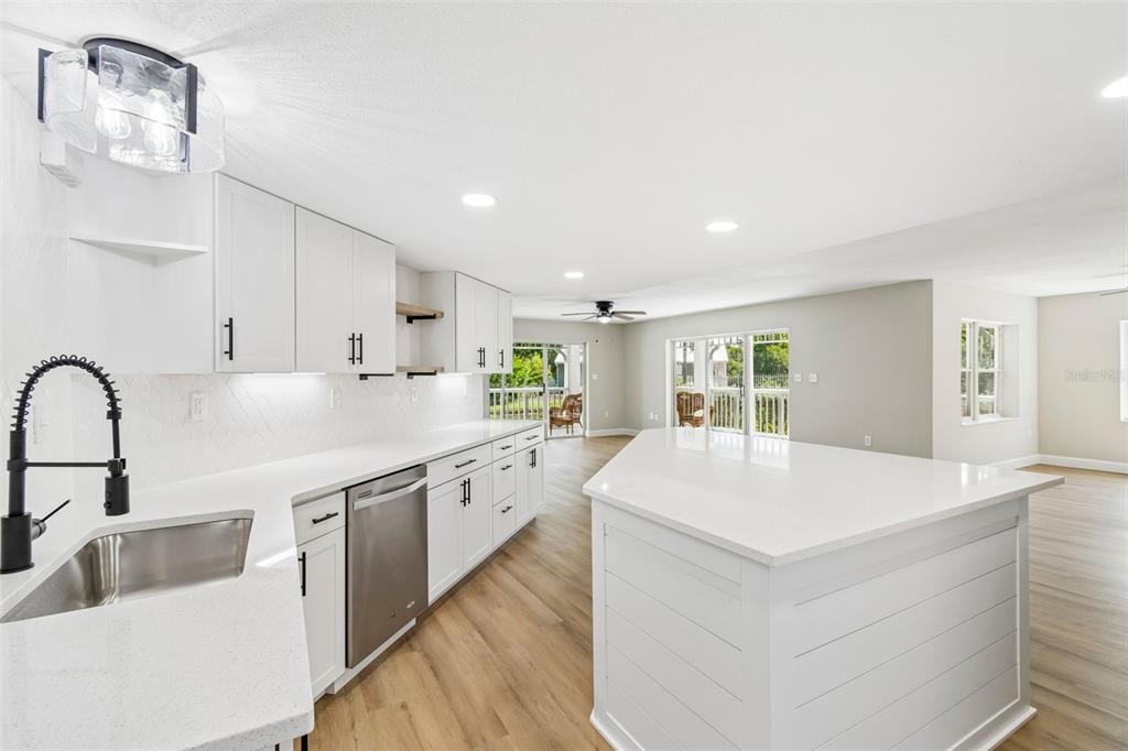 A modern kitchen features white cabinets, quartz countertops, a center island, and light wood flooring — 2533 DOLLY BAY DRIVE UNIT 101, PALM HARBOR, FL