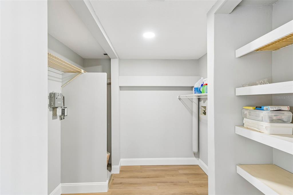 A laundry room features light gray walls, wood-look flooring, wire shelving, and built-in white shelves — 2533 DOLLY BAY DRIVE UNIT 101, PALM HARBOR, FL