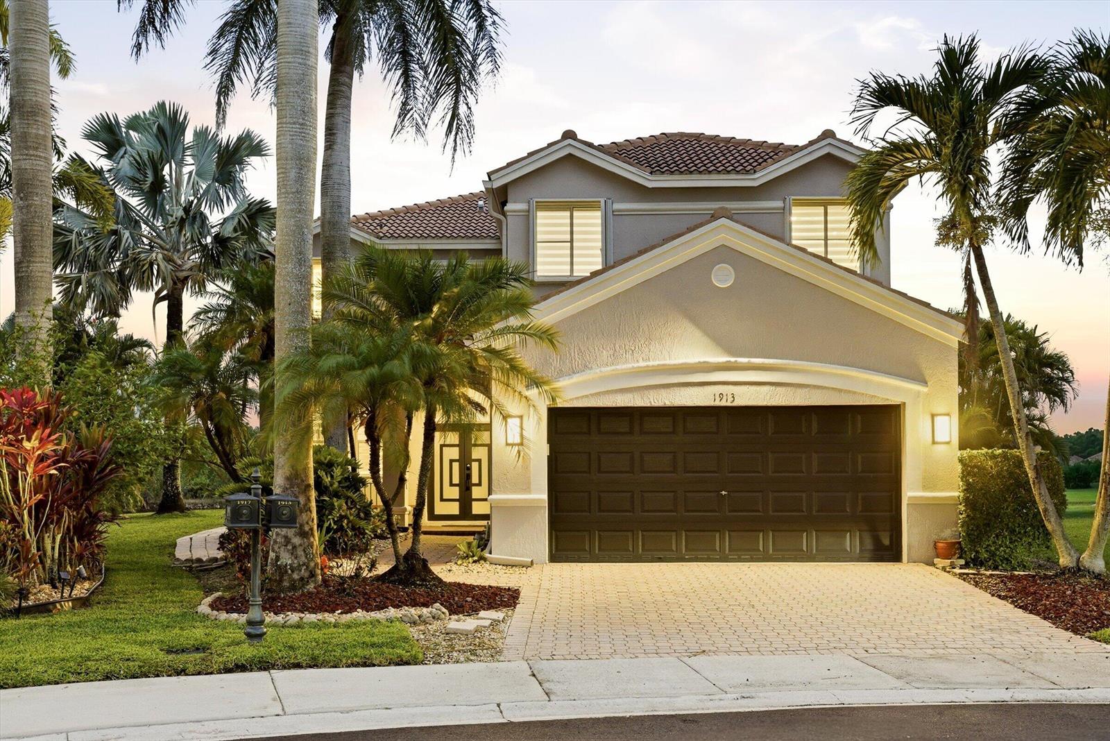 A two-story suburban house with a brown garage door, tiled roof, and surrounding palm trees — 1913 Silverbell Terrace, Weston FL 33327, WESTON, FL