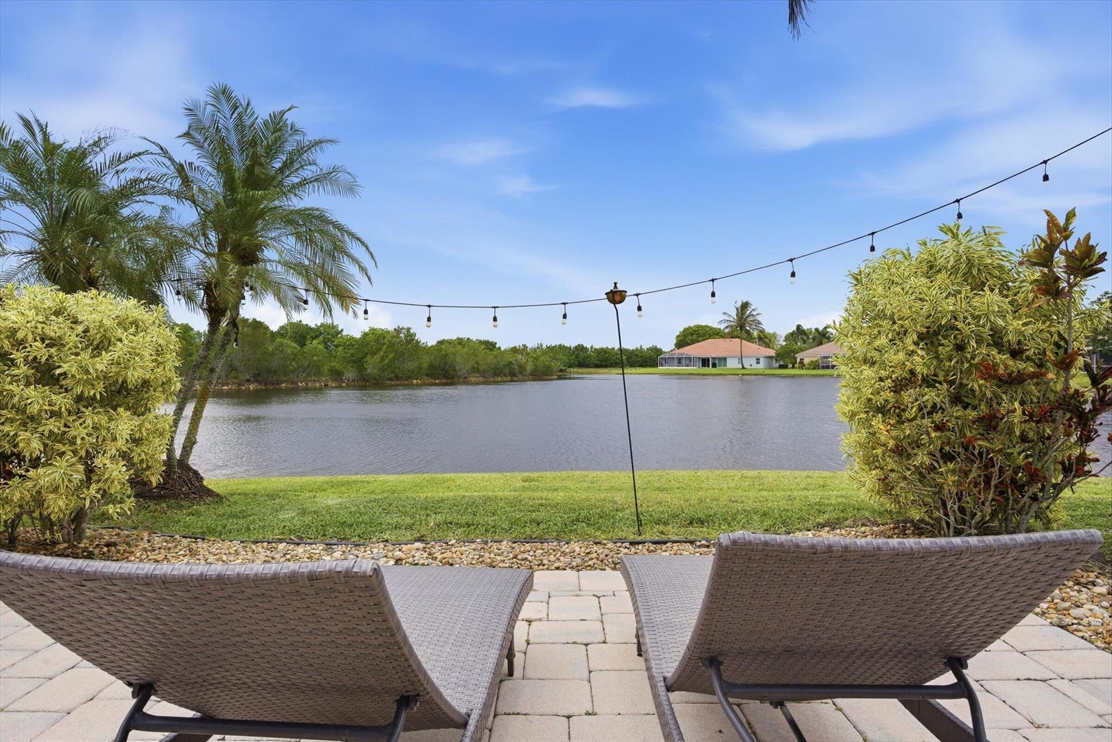 Two lounge chairs sit on a paved patio overlooking a lake with palm trees — 1913 Silverbell Terrace, Weston FL 33327, WESTON, FL