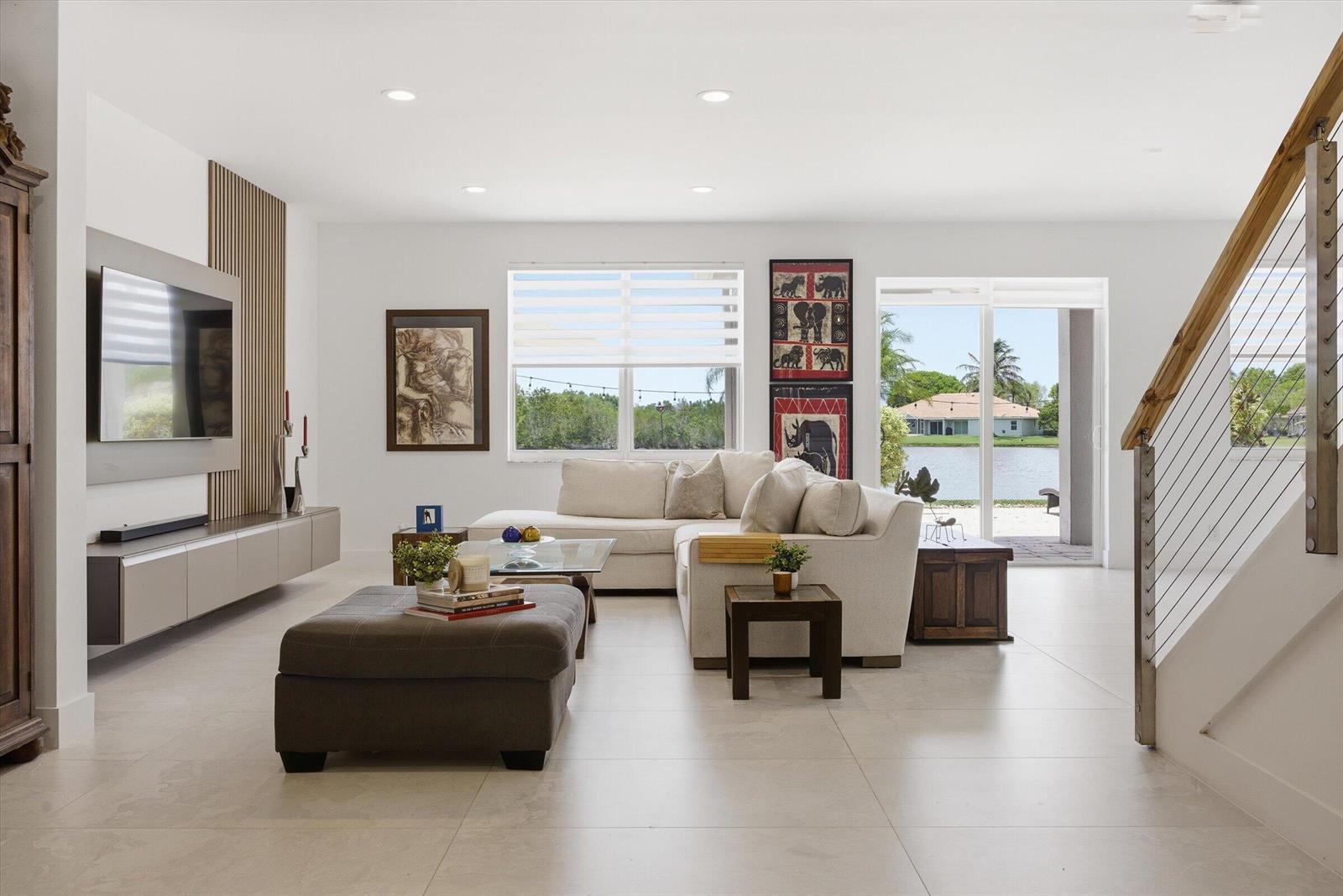 A modern living room features a sectional sofa, media console, and sliding doors overlooking water — 1913 Silverbell Terrace, Weston FL 33327, WESTON, FL