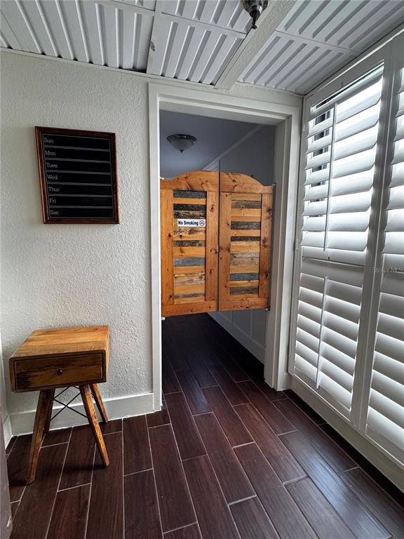 A room with wood-look tile flooring, a small wooden side table, and swinging saloon doors — 6165 CARRIER DRIVE UNIT 2702, ORLANDO, FL