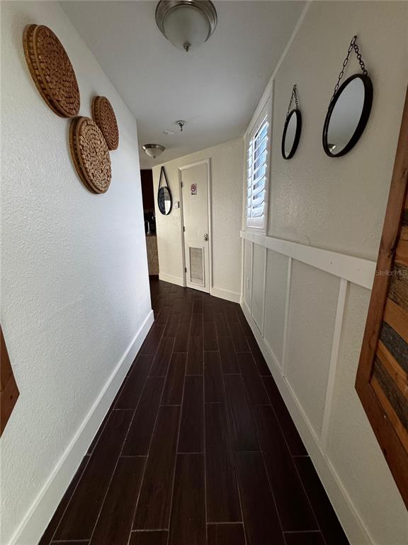 A hallway with dark wood-look tile flooring, white wainscoting, and wall-mounted circular decor — 6165 CARRIER DRIVE UNIT 2702, ORLANDO, FL