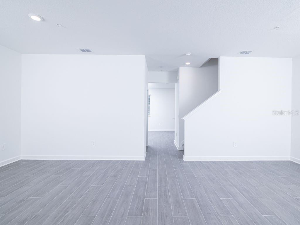 A bright, empty room features white walls, gray wood-look tile flooring, and a staircase — 11758 BOLDFACE DRIVE, ORLANDO, FL