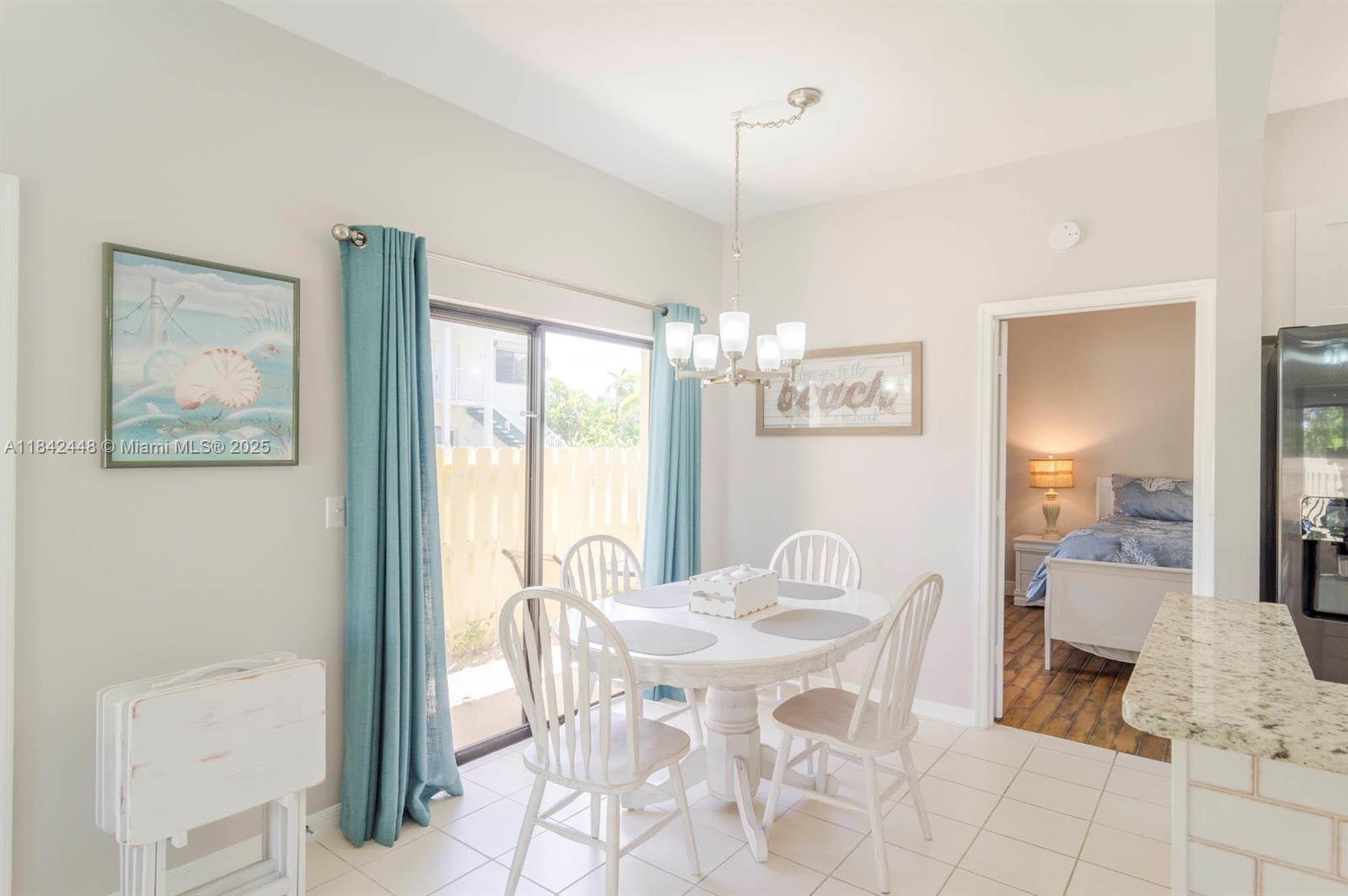 A dining area features a white round table, four chairs, a chandelier, and sliding glass doors — 720 S Bella Vista Ct S # 20, Jupiter FL 33477, JUPITER, FL