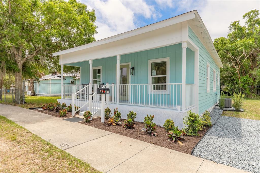 A light blue house with a front porch and white railings sits beside a sidewalk — 306 SHELDON STREET, NEW SMYRNA BEACH, FL