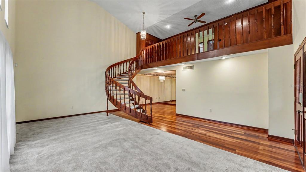 A living room features a curved wooden staircase, a loft balcony, and mixed carpet and flooring — 633 VICTORIA SQUARE LANE, LAKELAND, FL