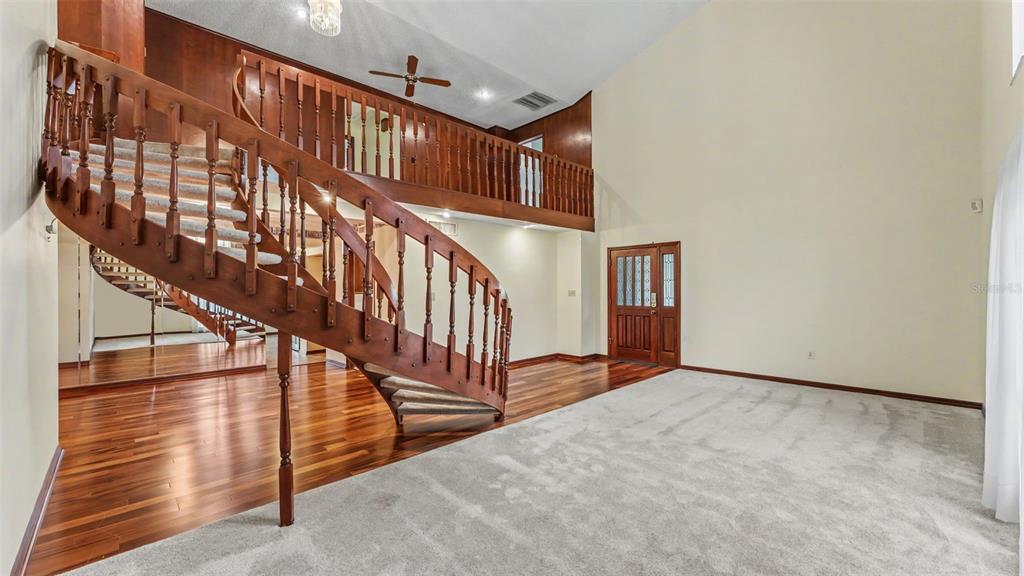 A spacious living room features a curved wooden staircase, a loft balcony, and carpeted flooring — 633 VICTORIA SQUARE LANE, LAKELAND, FL
